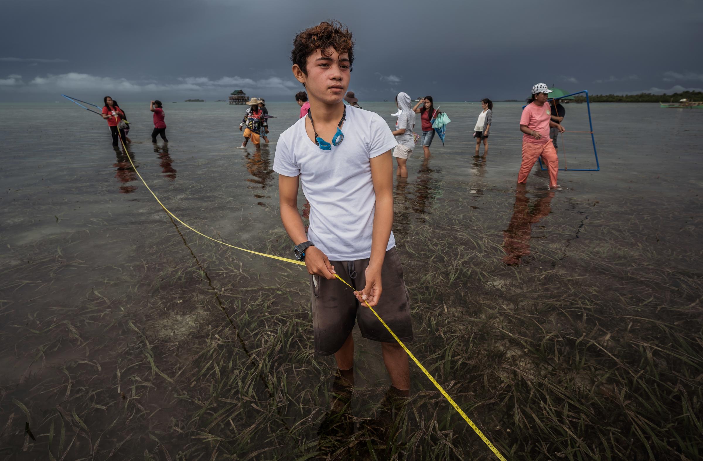 Ein Junge steht im Meer und hält ein Maßband um das Seegras im Küstenbereich zu vermessen. (Foto: Jakob Studnar) Ein Junge steht im Meer und hält ein Maßband um das Seegras im Küstenbereich zu vermessen. (Foto: Jakob Studnar)