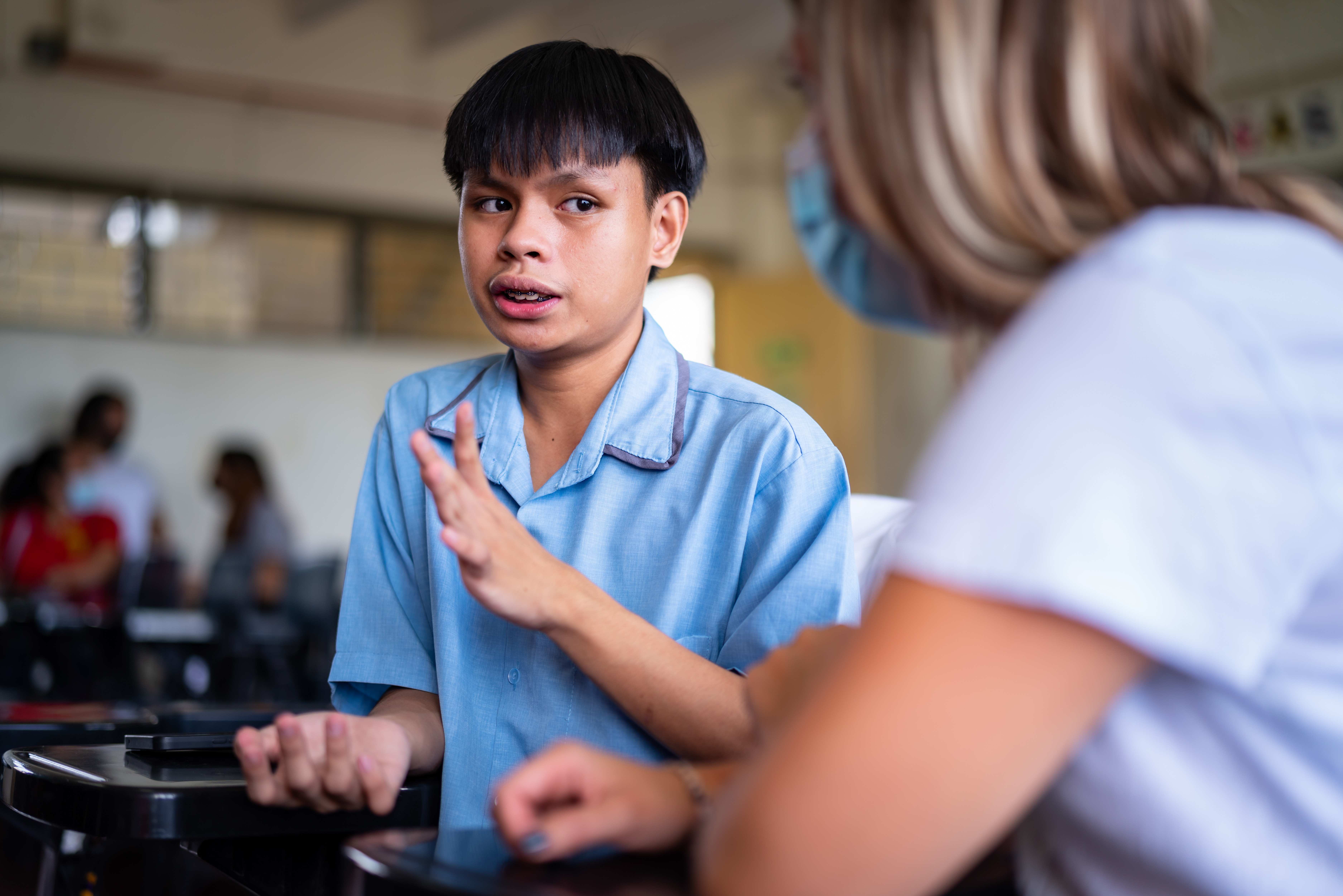 Ein Junge sitzt in einem Klassenraum und ist im Gespräch mit einer Mitatbeiterin der Kindernothilfe (Quelle: Jakob Studnar)