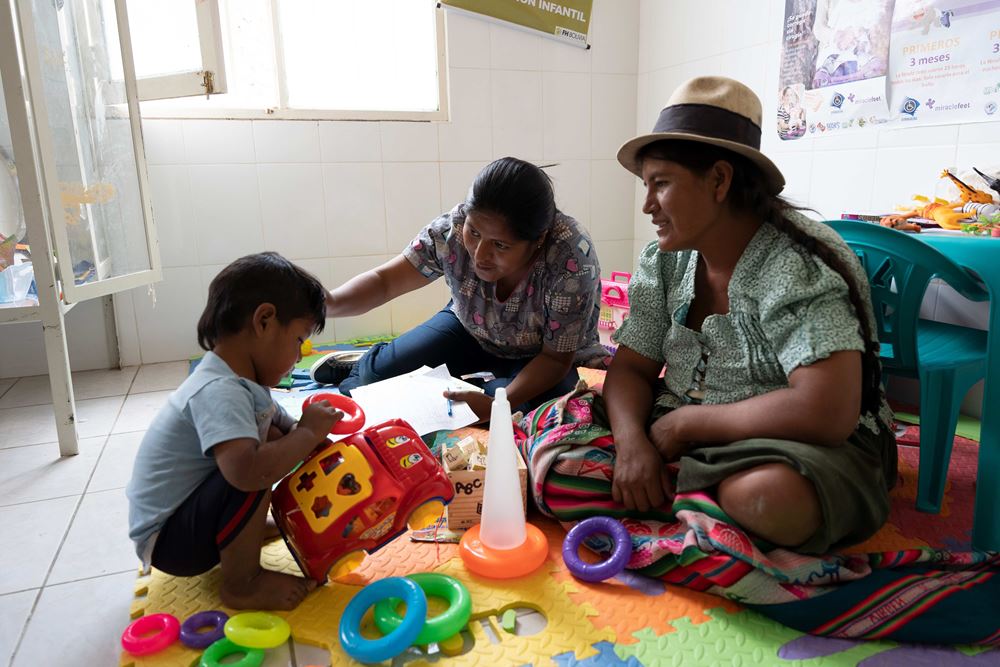 Bolivien, Gesundheitszentrum in Poroma: Ein kleiner Junge spielt, Mutter und Krankenschwester sitzen dabei (Quelle: Christian Nusch)