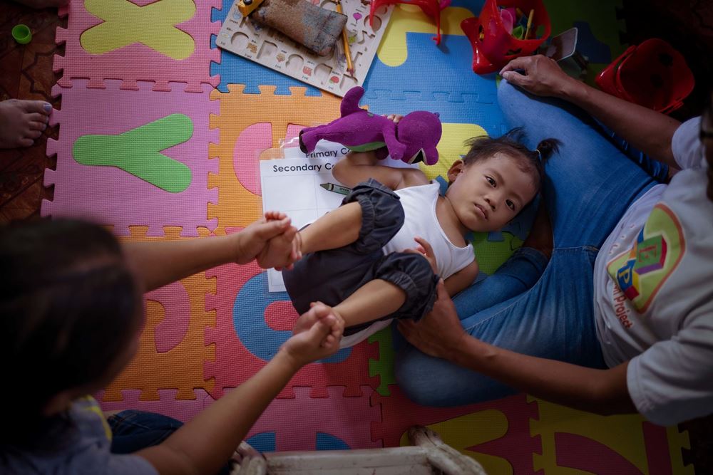 Ein Junge liegt auf einer bunten Matte und eine Frau macht Bewegungsübungen mit ihm (Quelle: Jakob Studnar) Ein Junge liegt auf einer bunten Matte und eine Frau macht Bewegungsübungen mit ihm (Quelle: Jakob Studnar)
