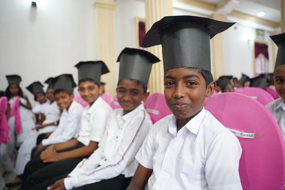 Einige Jungen mit weißen Oberhemden und schwarzen Doktorhüten sitzen in einer Reihe in einem Raum Die Buben sind sehr stolz auf ihren Abschluss (Foto: Christian Nusch)
