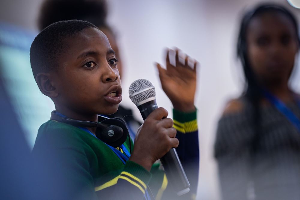 Ein Junge spricht in ein Mikrofon. Er hat an der Globalen Klimakonferenz in Kigali für arbeitende Kinder teilgenommen, die von der Kindernothilfe und terre des hommes organisiert wurde (Foto: Jakob Studnar) Ein Junge spricht in ein Mikrofon. Er hat an der Globalen Klimakonferenz in Kigali für arbeitende Kinder teilgenommen, die von der Kindernothilfe und terre des hommes organisiert wurde (Foto: Jakob Studnar)