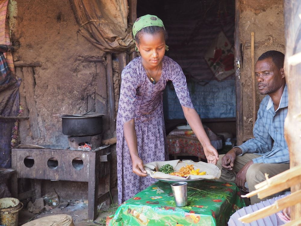 Ein äthiopisches Mädchen stellt ein Tablett mit Essen auf einem Tisch ab. (Quelle: Malte Pfau)