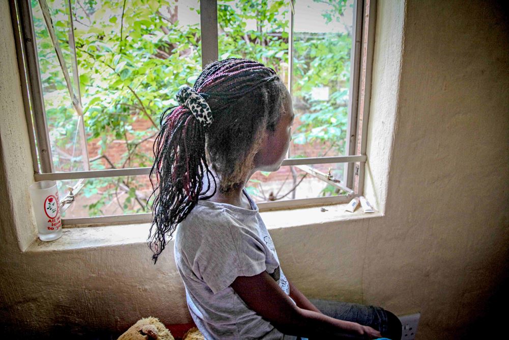 Ein Mädchen aus Südafrika blickt aus dem Fenster. Sie ist nur von hinten zu sehen, das Zimmer ist karg eingerichtet. (Quelle: Ralf Krämer)