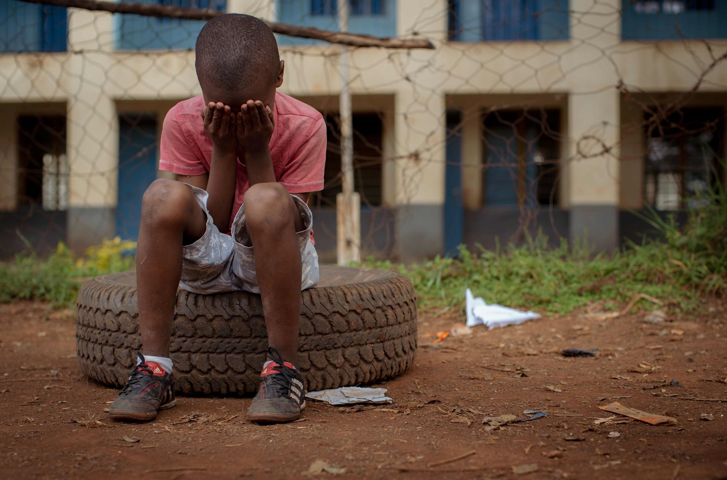 Ein Junge aus Kenia sitzt traurig  auf einem alten Autoreifen und vergräbt sein Gesicht in seinen Händen. (Quelle: Lars Heidrich)
